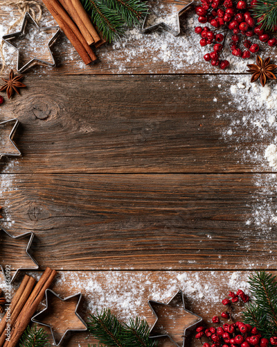 Cozy Christmas scene with cinnamon, pine, and red berries. Powdered sugar dusts rustic wooden planks. Star-shaped cookie cutters frame the composition