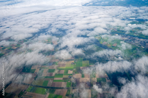 Aerial view of checkerboard-patterned agricultural fields in the Netherlands, dotted with wind turbines and partially covered by cumulus clouds.