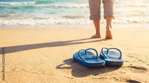 Flip-flops resting on sandy beach near walking person with footwear vacation sunshine shoreline lifestyle recreation tropical