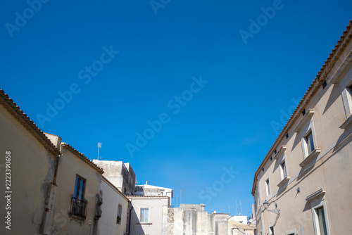 Facades of traditional light-colored stone buildings under a brilliant blue sky, characteristic of Mediterranean architecture in Sicily, with copy space
