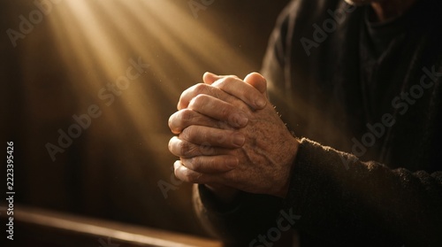 Hands clasped in prayer with warm light rays