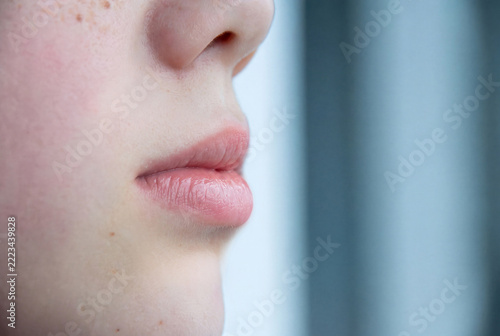 Close-up of natural pink lips with a glossy finish and slightly parted mouth. Detailed view of the lips, surrounding facial skin, and natural skin texture in soft lighting. Minimal makeup and realisti