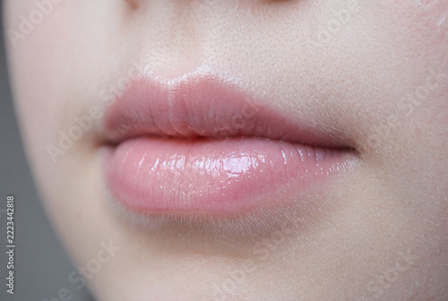 Close-up of natural pink lips with a glossy finish and slightly parted mouth. Detailed view of the lips, surrounding facial skin, and natural skin texture in soft lighting. Minimal makeup and realisti