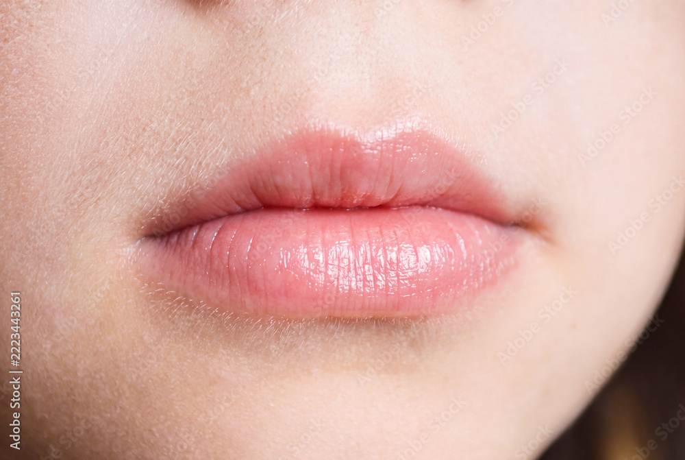 Obraz premium Close-up of natural pink lips with a glossy finish and slightly parted mouth. Detailed view of the lips, surrounding facial skin, and natural skin texture in soft lighting. Minimal makeup and realisti