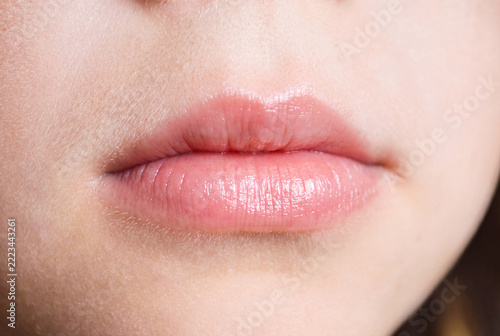 Close-up of natural pink lips with a glossy finish and slightly parted mouth. Detailed view of the lips, surrounding facial skin, and natural skin texture in soft lighting. Minimal makeup and realisti