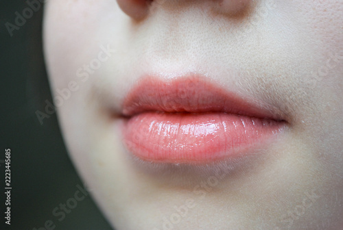 Close-up of natural pink lips with a glossy finish and slightly parted mouth. Detailed view of the lips, surrounding facial skin, and natural skin texture in soft lighting. Minimal makeup and realisti