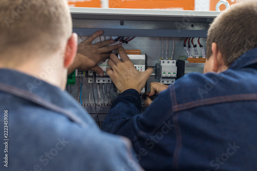 Team members work on electrical equipment inside a control panel at a technical facility during a training session