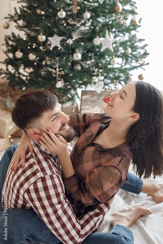 Romantic couple sitting near Christmas tree and hugging