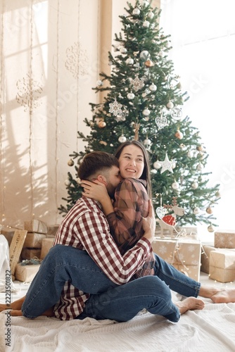Romantic couple sitting near Christmas tree and hugging