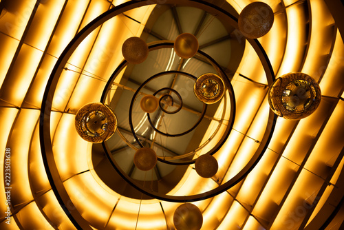 Low angle view of modern golden spiral staircase illuminated with warm ceiling lights and hanging decorative spheres.