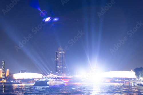Night view of Chao Phraya River with illuminated bridge, laser light show, and cruise boats in Bangkok.