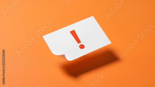 Exclamation mark on white paper note floating against vibrant orange background. Minimalist conceptual photography depicting urgent notice, important reminder, or attention alert for business projects