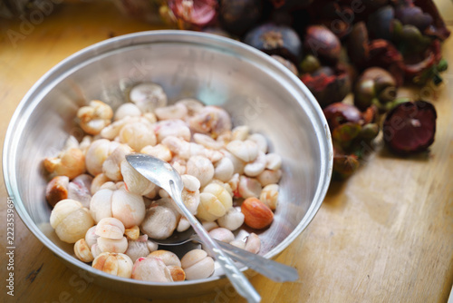 Fresh peeled mangosteen seeds in a metal bowl with spoons on a wooden table.