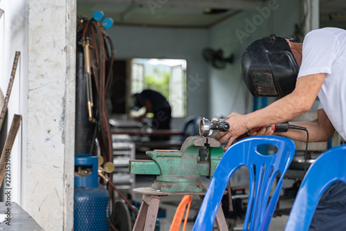 Worker in a Thai workshop grinding a coffee portafilter with a power tool, surrounded by industrial equipment.