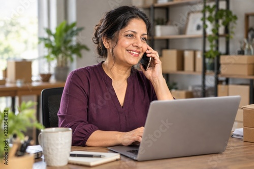 Smiling small business manager talking on a phone while working at her laptop