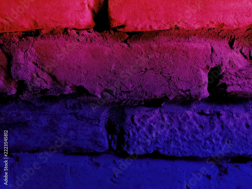 Vibrant bisexual pride flag colors painted across a rough textured urban brick wall with artistic pink purple and blue gradient lighting