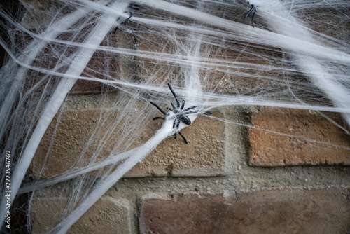 Black plastic spider trapped in stretched fake web on brick wall surface