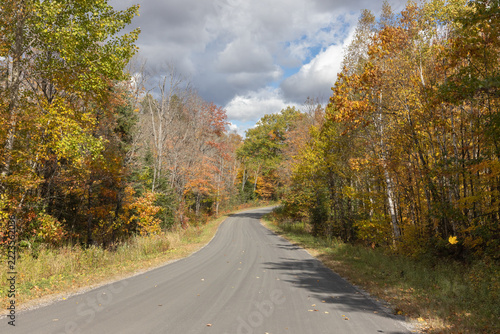 Road in northern Ontario with beautiful fall color and storm clouds clearing to show blue sky