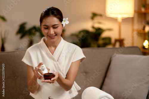Smiling Spa Therapist Pouring Natural Oil into Wooden Bowl in Cozy Living Room