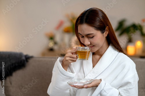 Young Woman in White Robe Drinking Herbal Tea While Relaxing at Home Spa