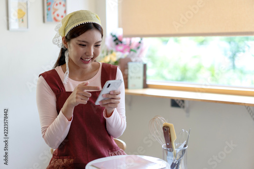Young Asian Woman Using Smartphone for Online Shopping While Baking in Bright Kitchen