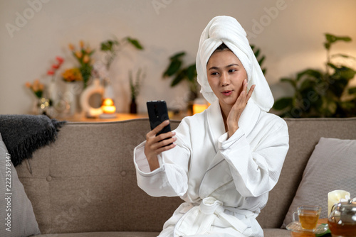Young Asian Woman in Robe with Towel Checking Skin on Smartphone at Spa