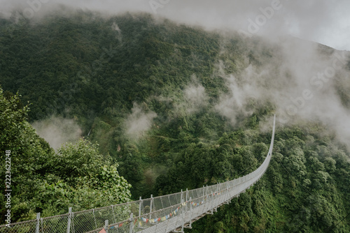 Suspension bridge with prayer flags over misty forest, Nepal