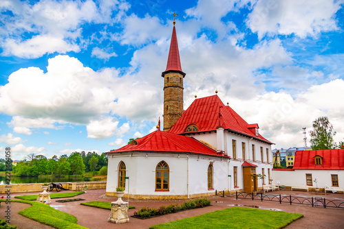 White church with red roof and spire stands serene. Lush green lawn surrounds its elegant architecture. Blue sky with fluffy clouds adds peaceful ambiance. , allowing undisturbed tranquility