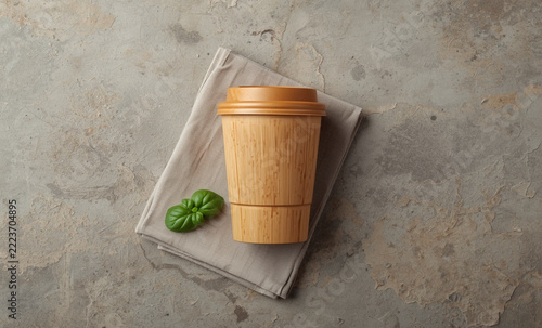 Reusable bamboo fiber coffee cup with napkin and green leaf flat lay on concrete surface