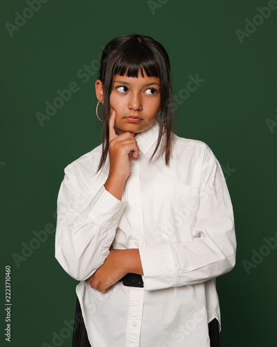 Thoughtful Teenage Girl Touching Chin and Smiling Gently Against Green Background