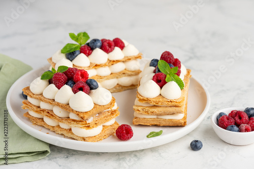 Delicious puff pastry Millefeuille dessert with white whipped cream, fresh organic berries, and mint leaves, selective focus.
