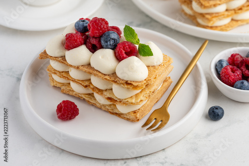 Delicious puff pastry Millefeuille dessert decorated with fresh berries and served with a golden fork on a light marble background. Selective focus