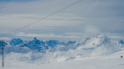 Panoramic snowy Caucasus mountain range with Mount Elbrus under overcast sky and foreground snow slope, distant jagged peaks and