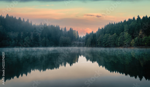 Karagol lake in Savsat, Artvin, Turkey, at dawn with a pink and orange sky, fog over the water and dark fir forest mirrored on the calm surface