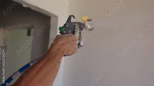 Worker applying plaster to interior wall using spray gun close up