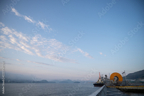 Wide morning sky and calm harbor pier with ship at dawn in June
