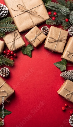 Kraft Paper Christmas Gifts with Pinecones and Red Berries Flat Lay on Red Background Concept