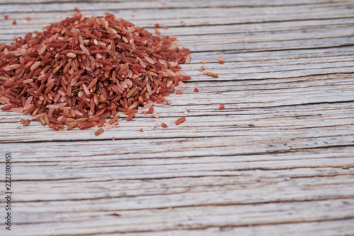 Red rice grains pile on weathered wooden surface. Texture contrasts between grain and wood add visual interest. Natural, rustic setting evokes wholesome, earthy qualities. Ideal for food, health