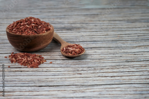 Red rice grains fill a rustic bowl and spoon. Wooden textures add warmth to the scene. Natural light highlights each grains rich hue. Ideal for health, nutrition, or cultural food themes