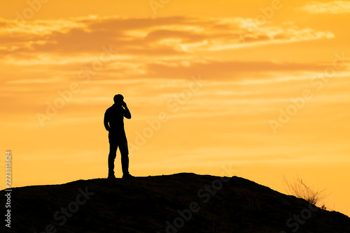 Silhouette of a man speaking on a mobile phone against a vibrant orange sunset backdrop