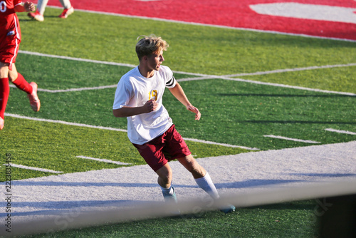 High School Boy's Varsity Soccer Player Running on a Turf Playing Field During a Game