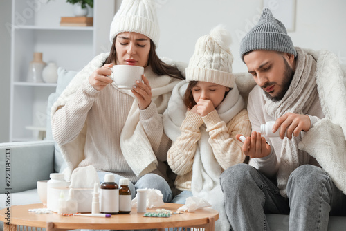 Ill family in warm hats treating cold on sofa at home