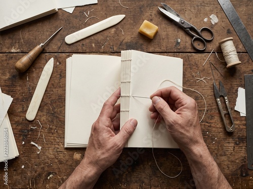 Bookbinder stitching blank pages at a worktable