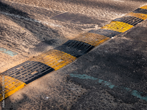 Worn Yellow and Black Speed Bump on Rough Textured Asphalt Road Surface
