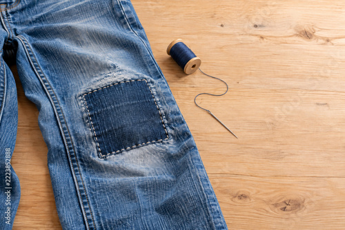 Repaired Blue Jeans with Denim Patch and Sewing Tools on Wooden Table