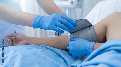Healthcare professional measuring a patient’s blood pressure with a cuff during routine medical examination in a hospital bed