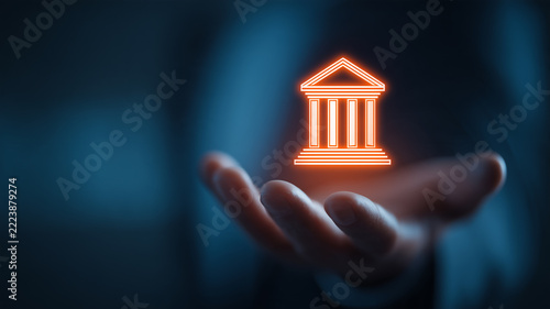 An open hand supporting a holographic bank building represents digital banking services and financial security in modern institutions.