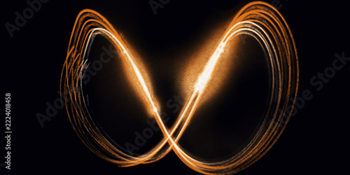 Glowing infinity symbol light painting on black background. Features luminous golden light trails forming a figure eight loop. Abstract photo for energy, connection, and technology themes.