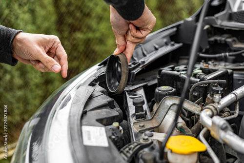Person holding round cap near car engine compartment outdoors