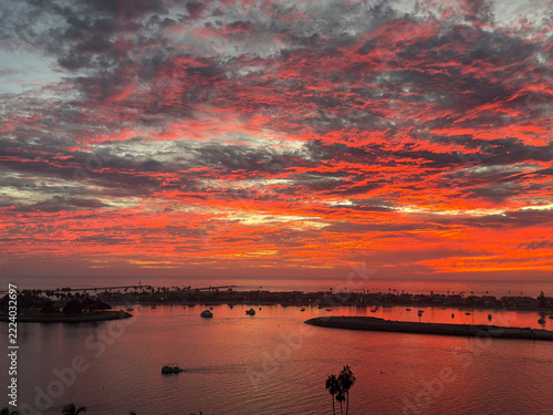 Vibrant red sunset sky reflecting on calm bay water at coastal harbor